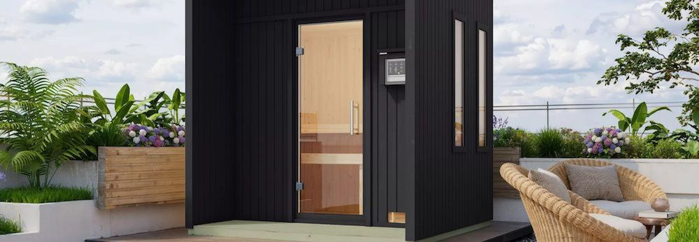 Eine dunklegraue Sauna von Karibu steht in einem Außenbereich
